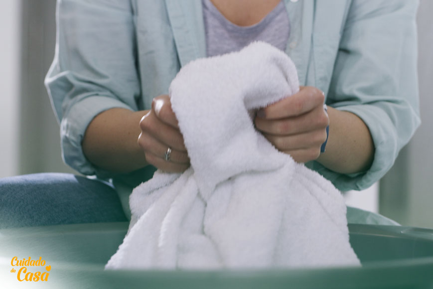 Mulher com uma toalha na mão na lavanderia escolhendo lava roupas líquido